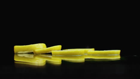 Slow-motion.-Sliced-​​lemon-rings-fall-with-splashes-of-water-on-the-glass-on-a-dark-background.-Cut-into-slices.
